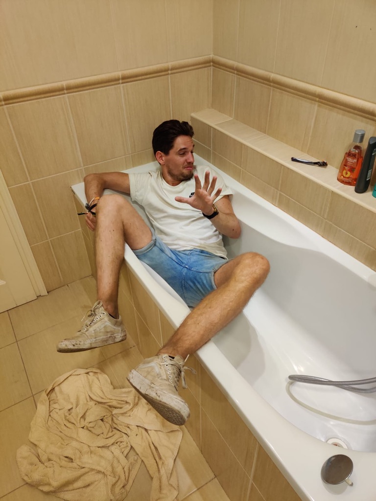 Tiemen zit volledig gekleed en met schoenen aan in een leeg bad